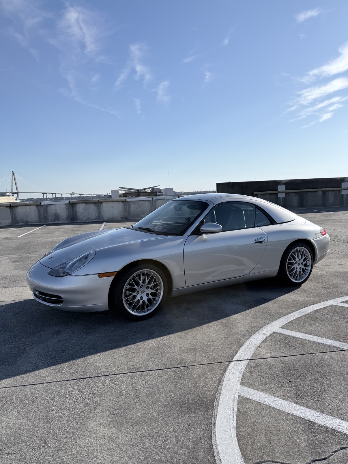 Wesley Neese's Arctic Silver 2001 Porsche 996 Carrera Cabriolet with factory hardtop, photographed on a Charleston rooftop with the Ravenel Bridge behind it.